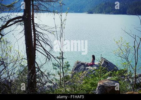 Mid adult woman, sitting on rock, in yoga position, rear view Stock Photo