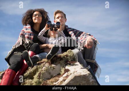Family sitting on rocks, boy using binolculars Stock Photo