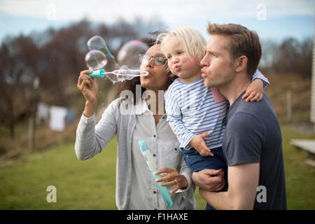 Mother blowing bubbles, father holding son Stock Photo