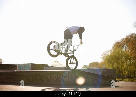 Young man doing stunt on bmx at skatepark, rear view Stock Photo