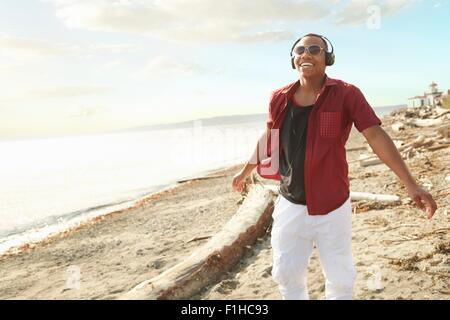 Young man standing on beach wearing headphones and sunglasses Stock Photo