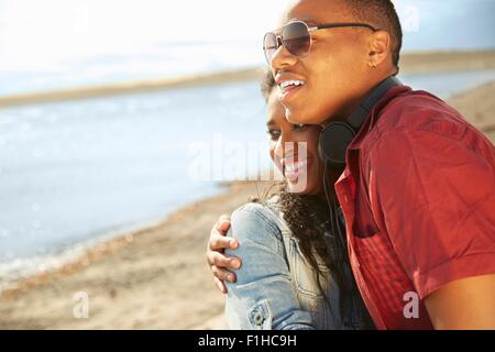 Young couple standing together on beach smiling, hugging looking away Stock Photo