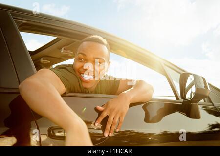 Young man leaning out of car window smiling Stock Photo