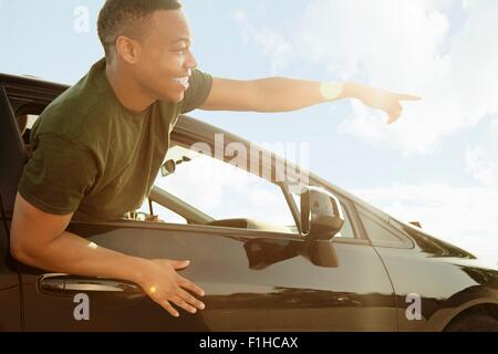 Young man leaning out of car window pointing and smiling Stock Photo