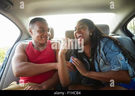 Young couple in car laughing, woman flexing muscles Stock Photo