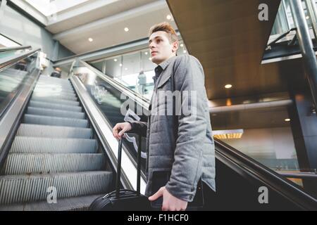 Young businessman commuter on escalator holding  suitcase handle. Stock Photo