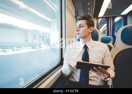 Portrait of young businessman commuter using digital tablet on train. Stock Photo