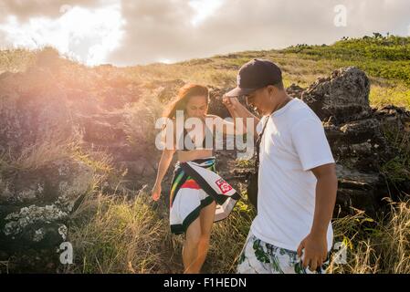 Young man giving girlfriend a helping hand on Makapuu coast path, Oahu, Hawaii, USA Stock Photo