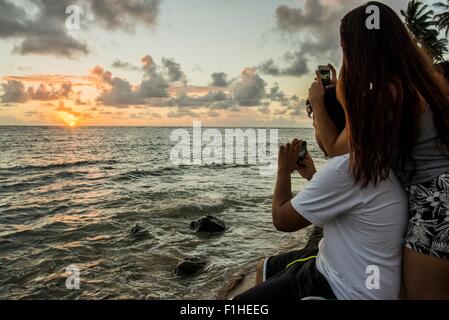 Couple photographing sunrise on smartphones, Kaaawa beach, Oahu, Hawaii, USA Stock Photo