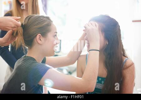 Four teenage girls doing each others hair and make up in bedroom Stock Photo