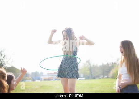 Teenage girl hoola hooping for friends in park Stock Photo