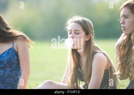 Teenage girl blowing bubble gum bubble in park Stock Photo