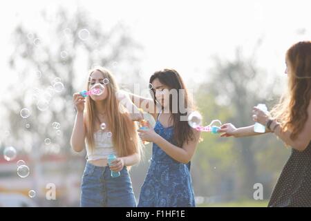 Three teenage girls blowing bubbles with bubble wand in park Stock Photo