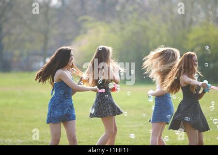 Four teenage girls spinning bubbles with bubble wand in park Stock Photo