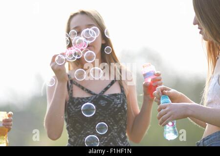 Two teenage girls blowing bubbles in park Stock Photo