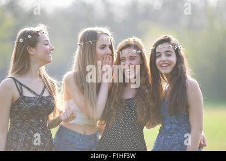 Four teenage girls wearing daisy chain headdresses giggling in park Stock Photo