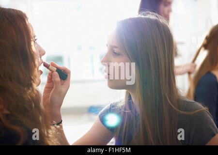 Teenage girl having lipstick applied by best friend in bedroom Stock Photo