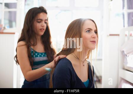 Teenage girl having hair plated by best friend in bedroom Stock Photo