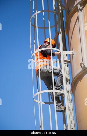 Worker climbing smoke stack ladder Stock Photo