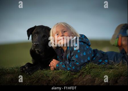 Young boy lying down with dog in field Stock Photo