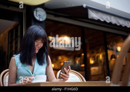 Young woman, sitting outside cafe, using smartphone, Shanghai, China Stock Photo