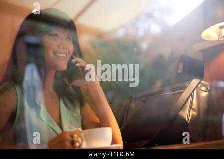 Young woman drinking coffee in cafe, using smartphone, Shanghai, China Stock Photo