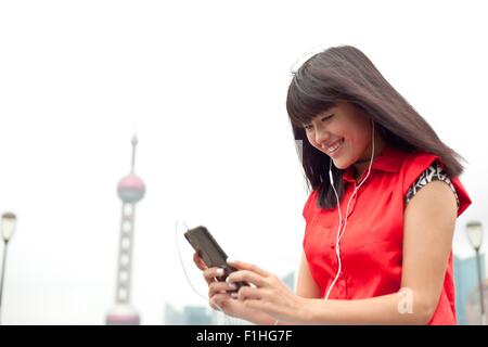 Young woman wearing earphones, looking at smartphone, Shanghai, China Stock Photo