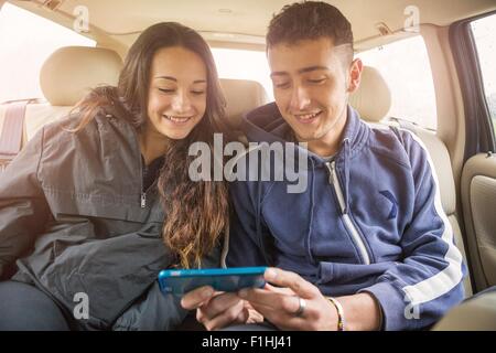 Teenage girl and young man reading smartphone text in car back seat Stock Photo
