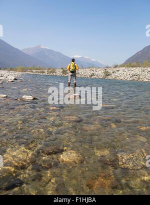 Rear view of young male hiker crossing Toce river, Vogogna, Verbania, Piemonte, Italy Stock Photo