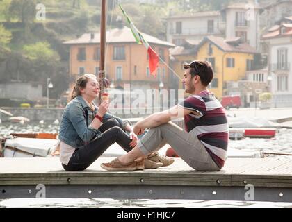 Couple sitting on pier eating ice cream cone at lake Mergozzo, Verbania, Piemonte, Italy Stock Photo