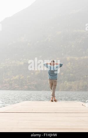 Rear view of young man looking out from pier, Lake Mergozzo, Verbania, Piemonte, Italy Stock Photo