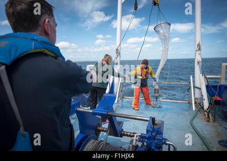 Marine biologists taking samples from plankton net on research ship