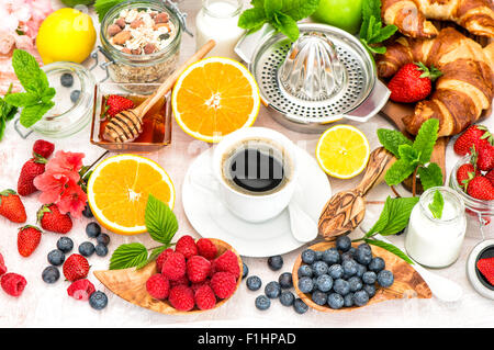 Breakfast with coffee, croissants, granola, honey, fresh berries, fruits orange, apple, milk. Stock Photo