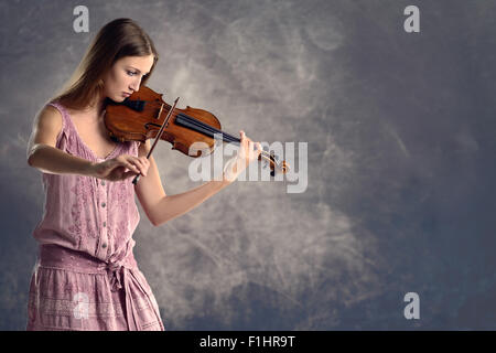 Pretty young female violinist in a stylish pink outfit standing playing the violin as she gives a classical recital at the acade Stock Photo