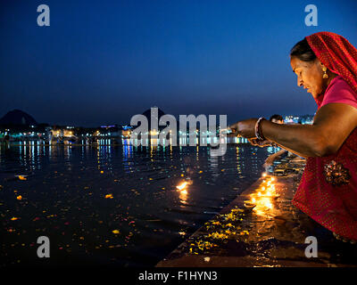 An Indian female with a plate of fire against Holy Pushkar Lake at evening against blue sky Stock Photo