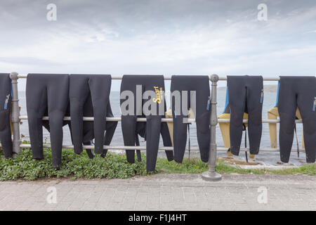 Eight wetsuits draped over a rail on the roadside in Sennen Cove, Cornwall, a noted surfing and watersports area. UK Stock Photo