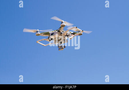 Camouflage Quadrocopter hovering  against a blue sky with landing gear up Stock Photo