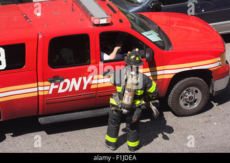 FDNY Firefighter in full turnout gear speaks with his supervisor in a red pickup truck on the street. Stock Photo