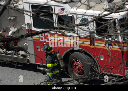 NYFD Firefighter in full turnout gear walking past Firetruck 93 parked on the street as seen through tree branches Stock Photo