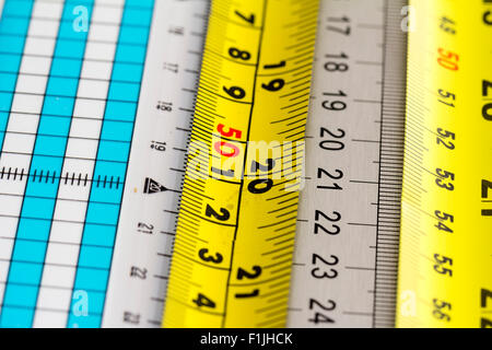 Overhead view of several different rulers and metal tape measures. Yellow tape measure, with white, grey and other rulers. Stock Photo