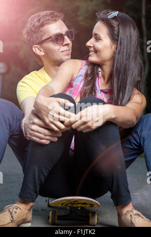Young happy couple in love sitting on a skateboard outdoors Stock Photo