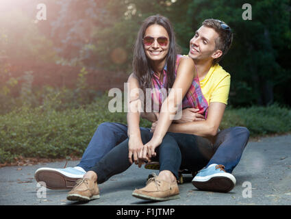 Young happy couple in love sitting on a skateboard outdoors Stock Photo