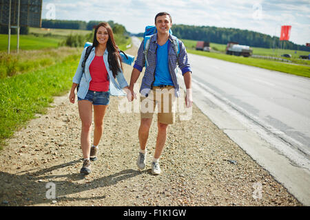 Young hikers with backpacks walking along highway Stock Photo