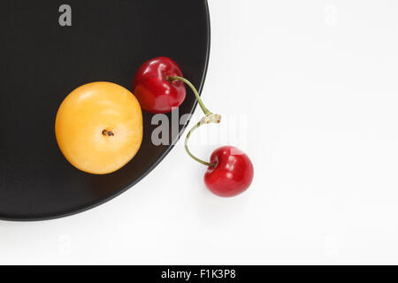Yellow plum and red cherries on black plate Stock Photo