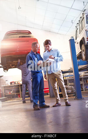Mechanic with clipboard talking to customer in auto repair shop Stock Photo