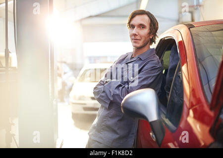 Portrait confident mechanic leaning on car in auto repair shop Stock Photo