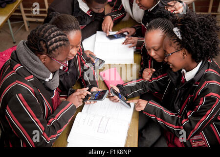 Four school girls sit around a table while working on their calculators Stock Photo