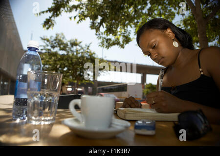 Woman writing in diary at coffee shop. Newtown, Johannesburg, Gauteng, South Africa Stock Photo