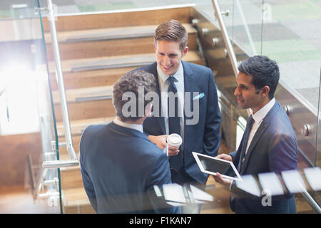 Businessmen with digital tablet and coffee talking on stairs Stock Photo
