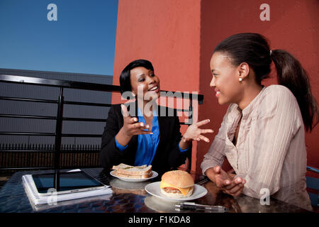 Two female colleagues talk over lunch, smiling Stock Photo